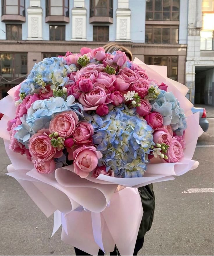 a woman holding a bouquet of pink and blue flowers in front of a large building