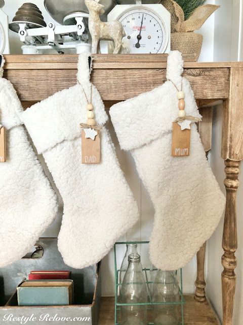 two white christmas stockings hanging from a mantel in front of a clock and other decorations