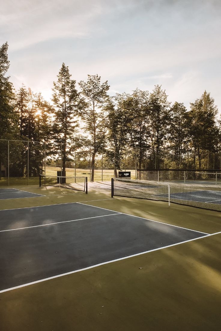 an outdoor tennis court with trees in the background and sun shining on the ground behind it