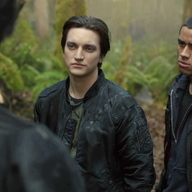 two young men standing next to each other in front of trees and ferns on a foggy day