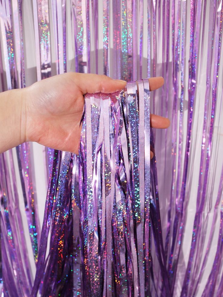 someone is holding some purple streamers in front of the curtain that has sequins on it