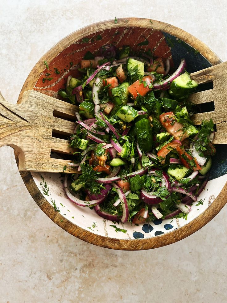 a salad in a bowl with two wooden utensils