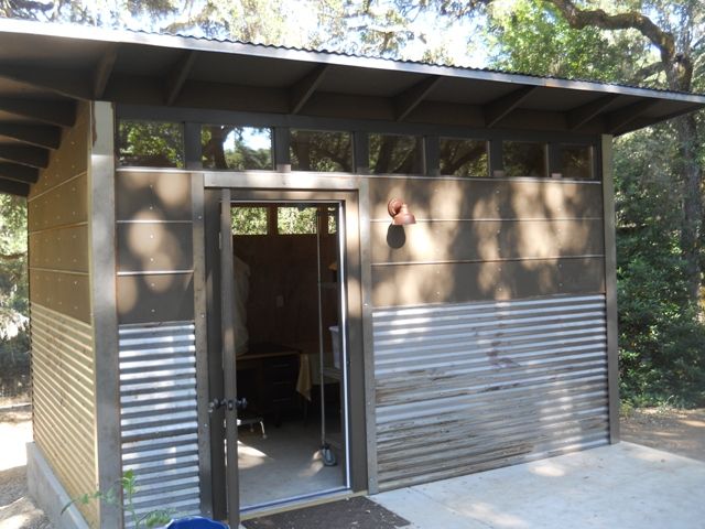 a metal shed with the door open to let in some light and shade from the trees