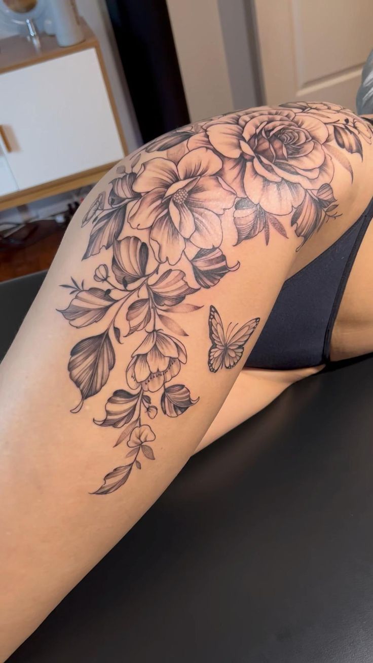 a woman laying on top of a black table next to a flower and butterfly tattoo