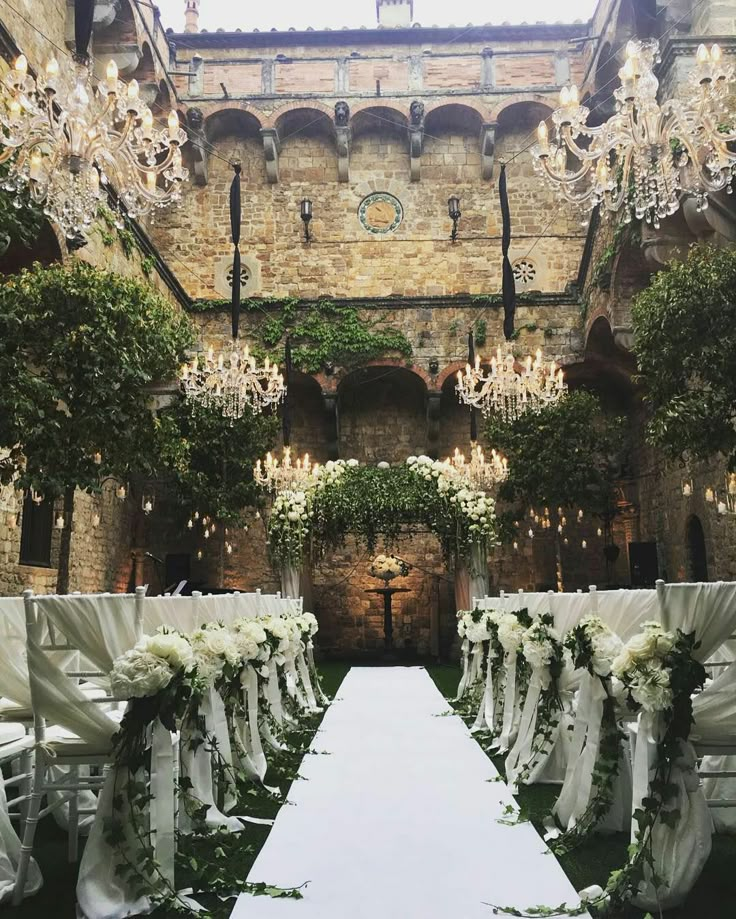 the aisle is lined with white flowers and greenery, along with chandeliers