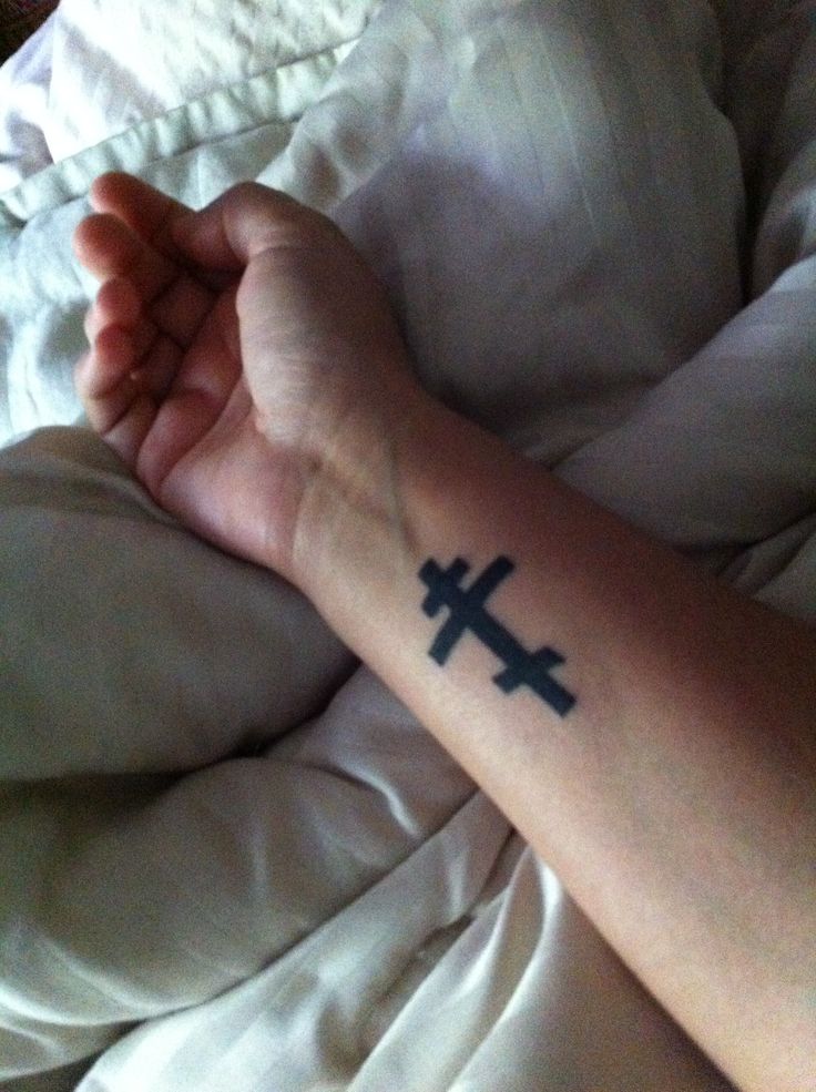 a person laying in bed with a cross tattoo on their arm and hand behind them