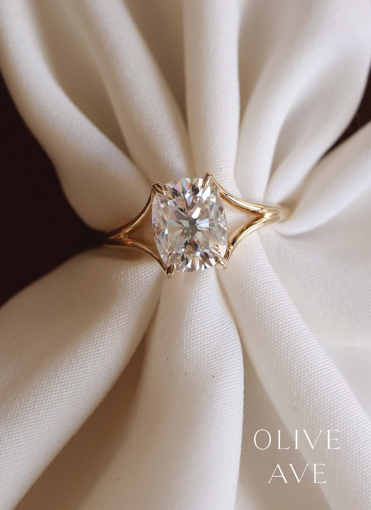 a diamond ring sitting on top of a white cloth covered napkin with the words olive ave written below it