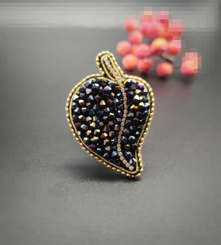 a black heart shaped brooch sitting on top of a table next to some beads