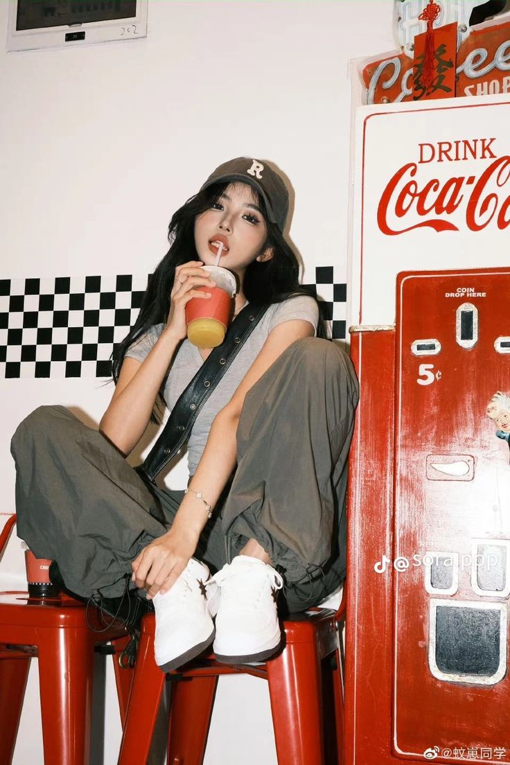 a woman sitting on top of a red stool next to a coca - cola machine