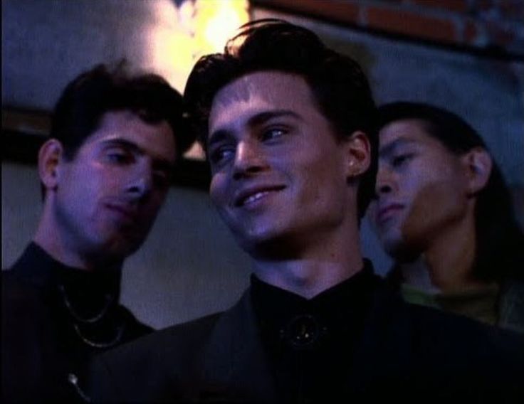 three young men standing next to each other in front of a brick wall with lights on