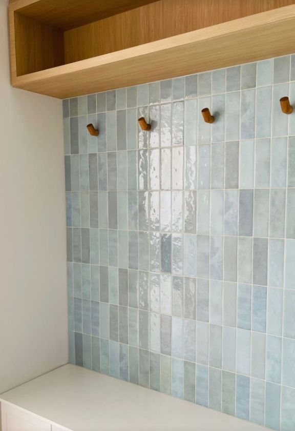 a kitchen with blue tiles on the backsplash and wooden shelf above it,