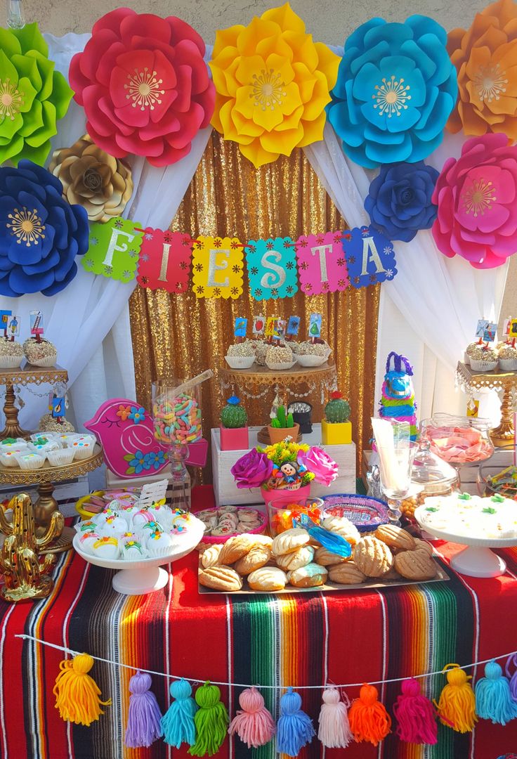 a colorful dessert table with paper flowers and tassels