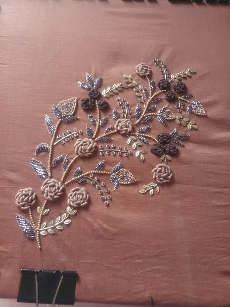 a piece of cloth with flowers and leaves embroidered on the side, sitting on a table