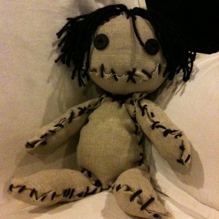 a close up of a stuffed animal on a bed with white sheets and black hair