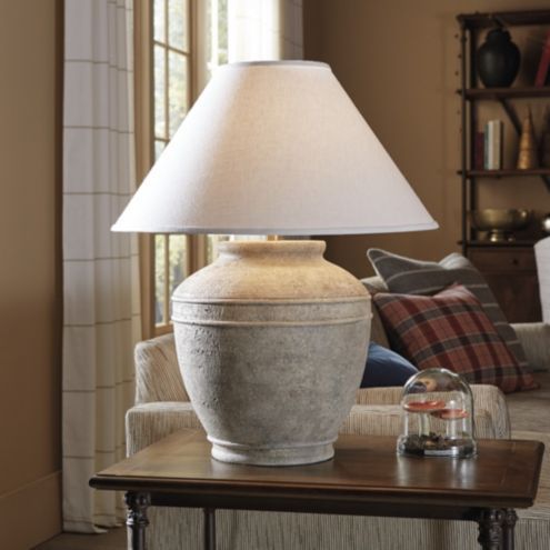 a table lamp sitting on top of a wooden table in front of a couch and window