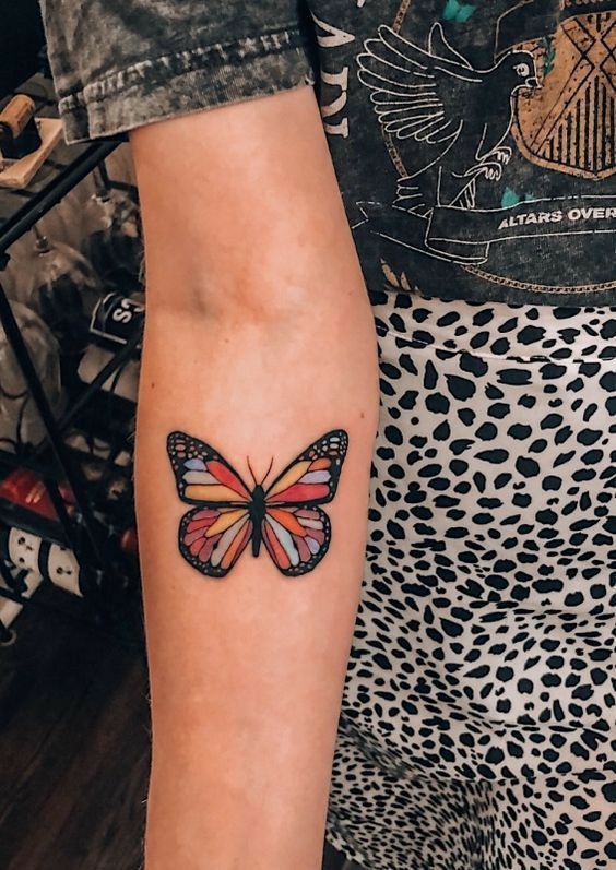 a woman's arm with a colorful butterfly tattoo on the left side of her arm