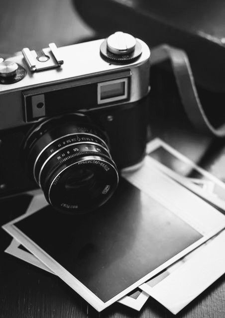 an old fashioned camera sitting on top of several polaroid photos next to a brown leather bag