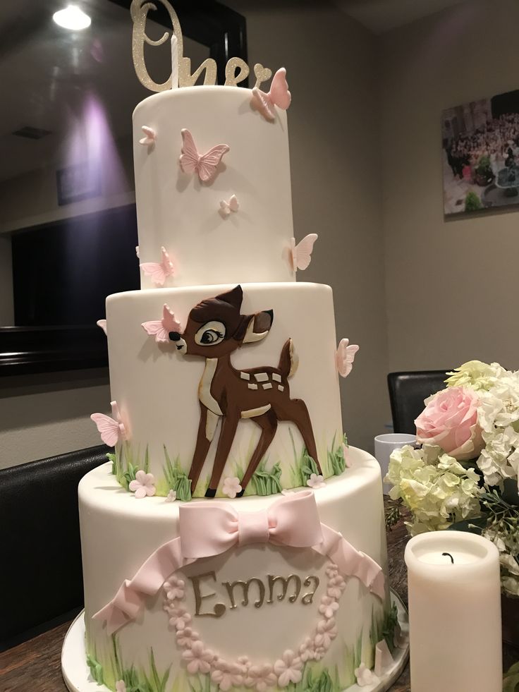 a three tiered cake decorated with pink flowers and deer on the side, sitting on top of a table