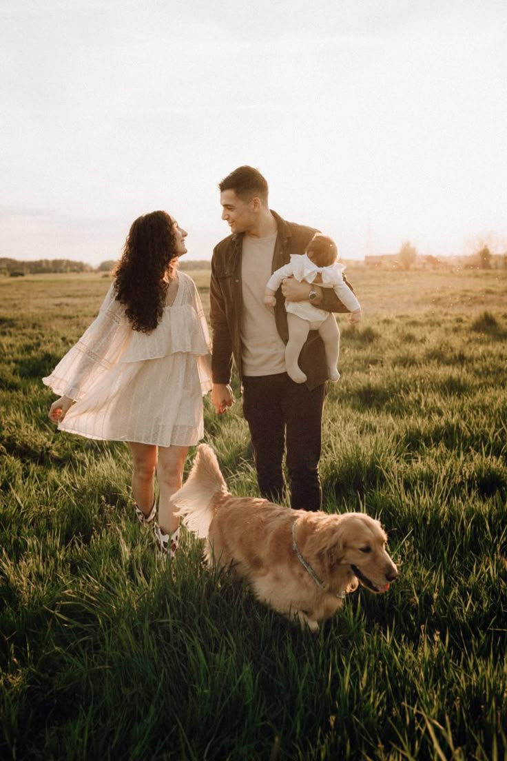 a man and woman holding hands while walking with a dog in the middle of a field