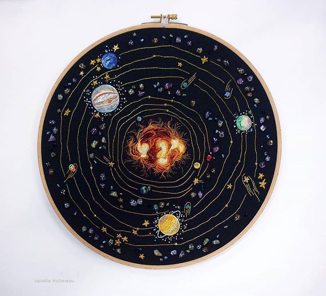 an embroidery project with planets and stars in the center on a white wall behind it