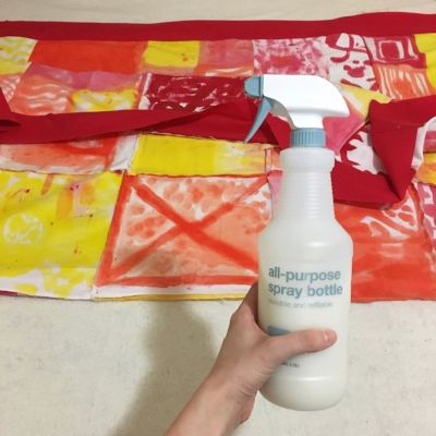 a hand holding a spray bottle with red and yellow squares on it next to a quilt