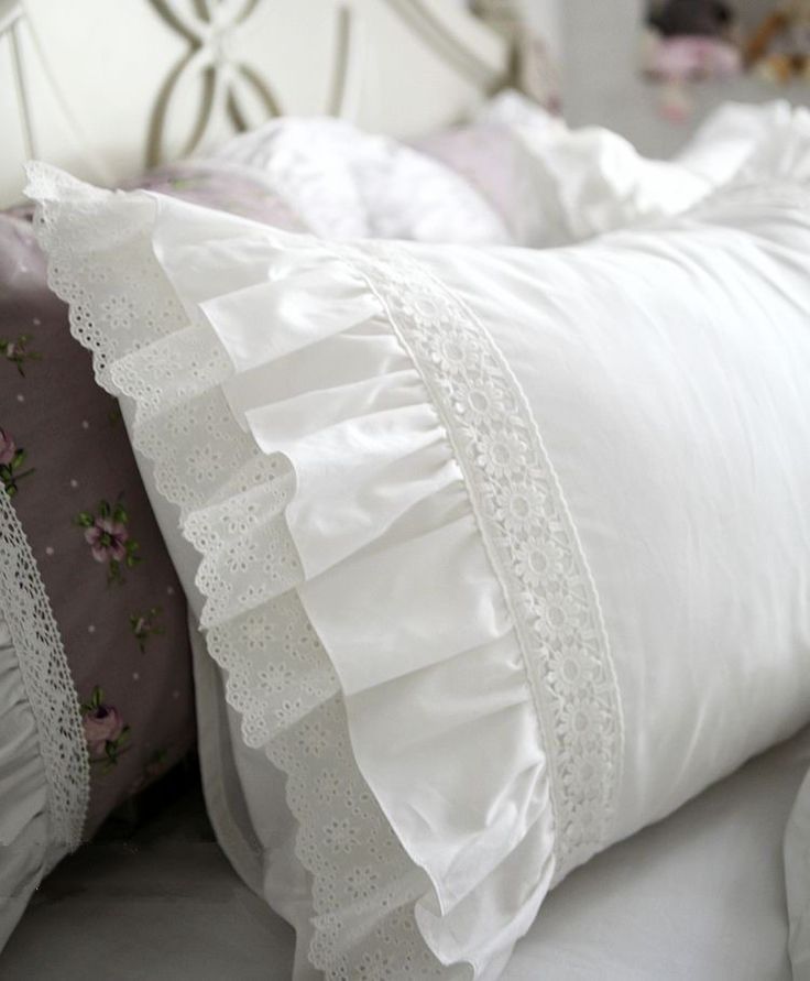 a white bed topped with lots of pillows and ruffles on top of it