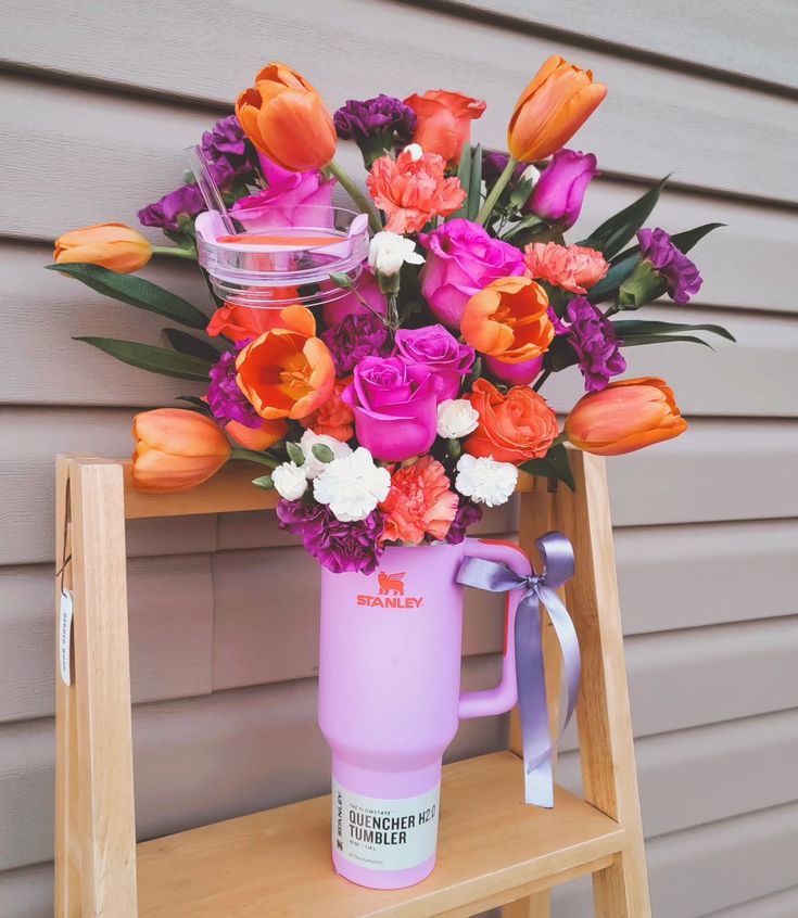 a pink coffee cup with flowers in it sitting on a wooden shelf next to a wall