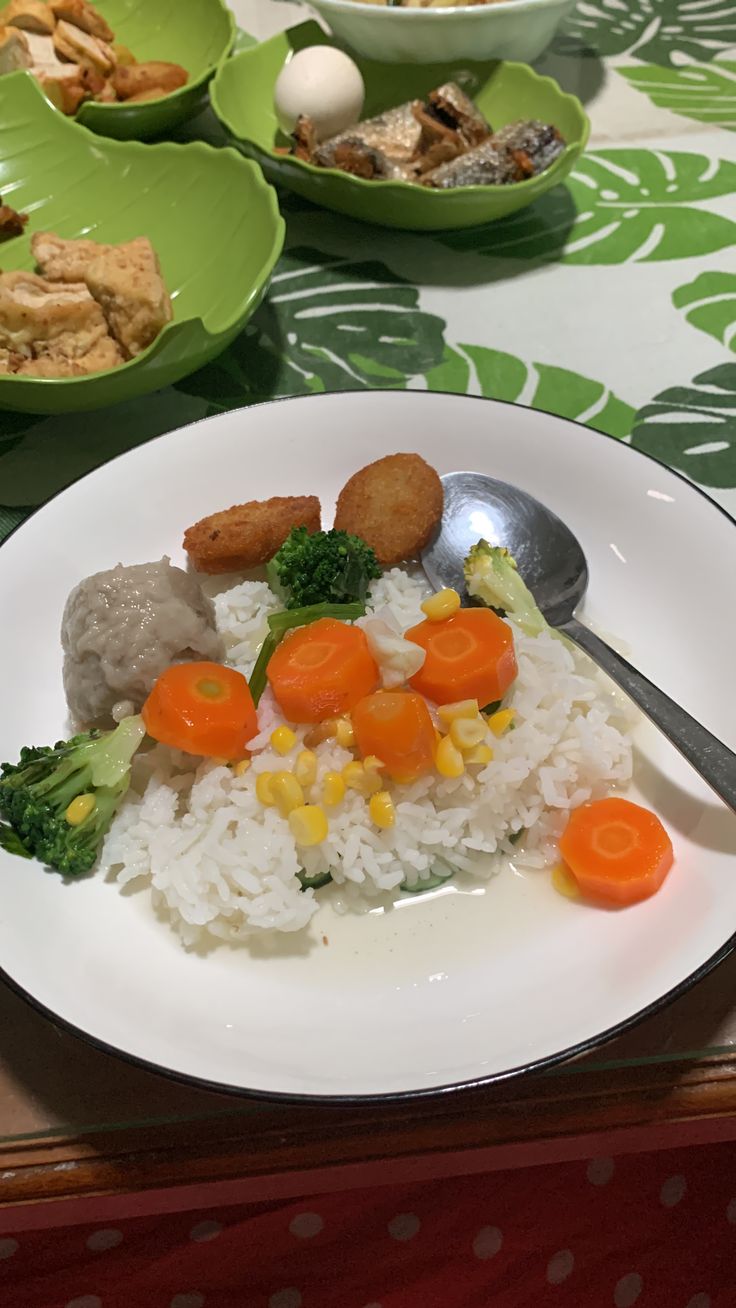 a white plate topped with rice and veggies next to bowls of food on a table