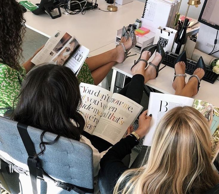 three women sitting at a table with books in front of them and one reading a magazine