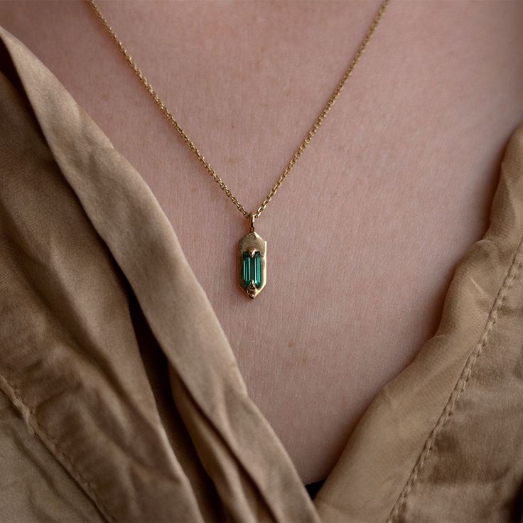 With its modern, understated style, wear this emerald set Amulet necklace for a hint of sparkle and casual luxe. Hanging from the center of the 14K yellow gold chain is a hexagon shaped pendant with two claw prongs that hug a mesmerizing green baguette cut emerald. The best part about this pendent is that it is 100% cu Yellow Gold Necklace With Emerald Rectangular Pendant, 14k Gold Emerald Cut Birthstone Necklaces, Dainty Emerald Cut Yellow Gold Necklace, Emerald Cut Birthstone Necklace In 14k Gold, 14k Gold Emerald Cut Birthstone Necklace, Minimalist Emerald Necklace In Yellow Gold, Minimalist 14k Yellow Gold Emerald Necklace, Minimalist 14k Gold Emerald Gemstone Necklace, 14k Gold Octagon Gemstone Necklace