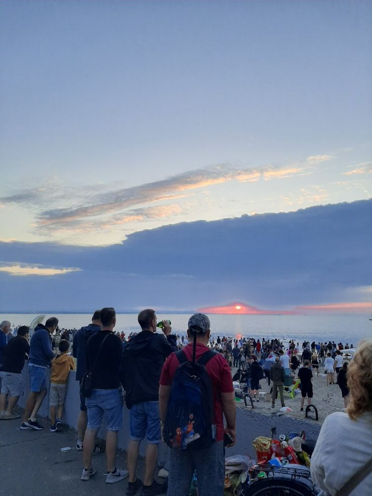 a group of people standing on top of a beach next to the ocean at sunset