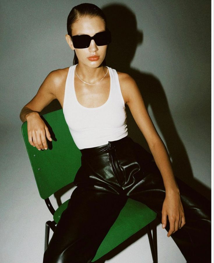 a woman in black leather pants and sunglasses sitting on a green chair with her legs crossed