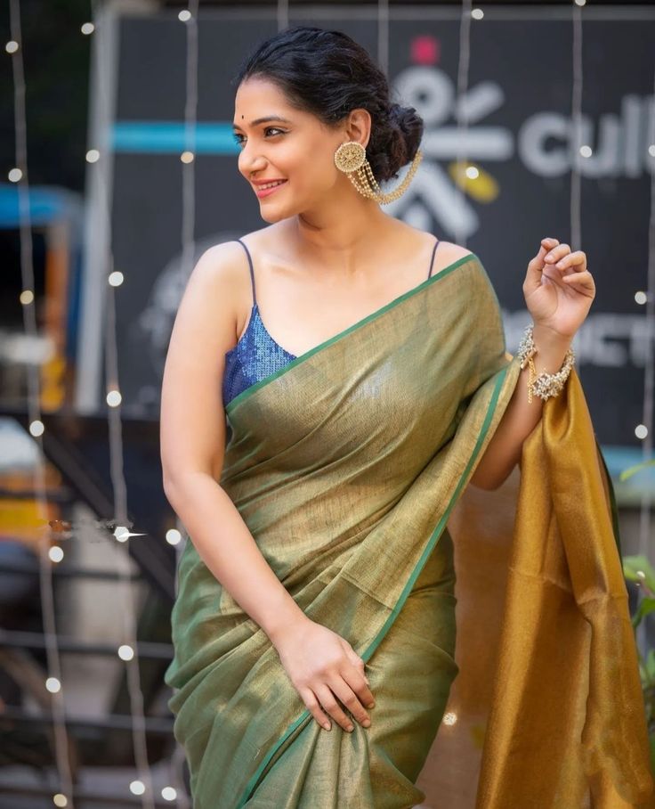 a woman in a green and gold sari is smiling at the camera with her hand on her hip