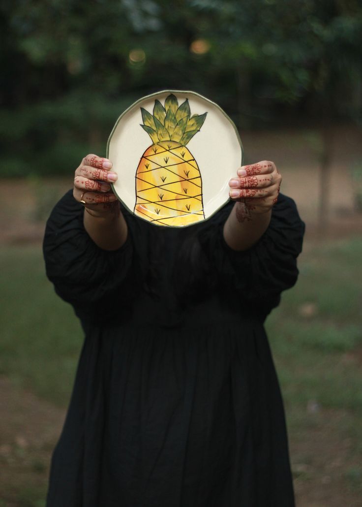 a woman holding up a plate with a painted pineapple on it