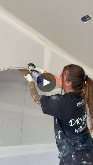 a woman is painting the ceiling with white paint and she has her hair in pigtails