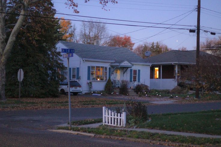 a white house sitting on the side of a road next to a tree filled street