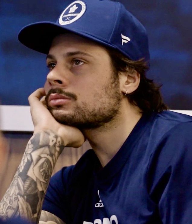 a man with long hair wearing a baseball cap and holding his hand to his face