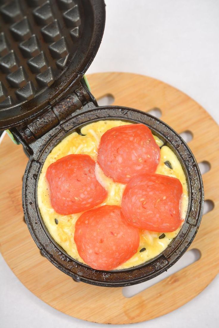 an omelet with sausages in it sitting on a cutting board next to a waffle iron