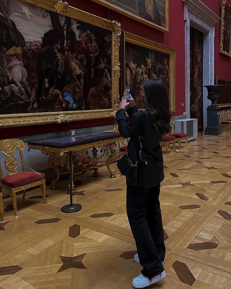 a woman taking a photo in an ornate room with paintings on the walls and floor