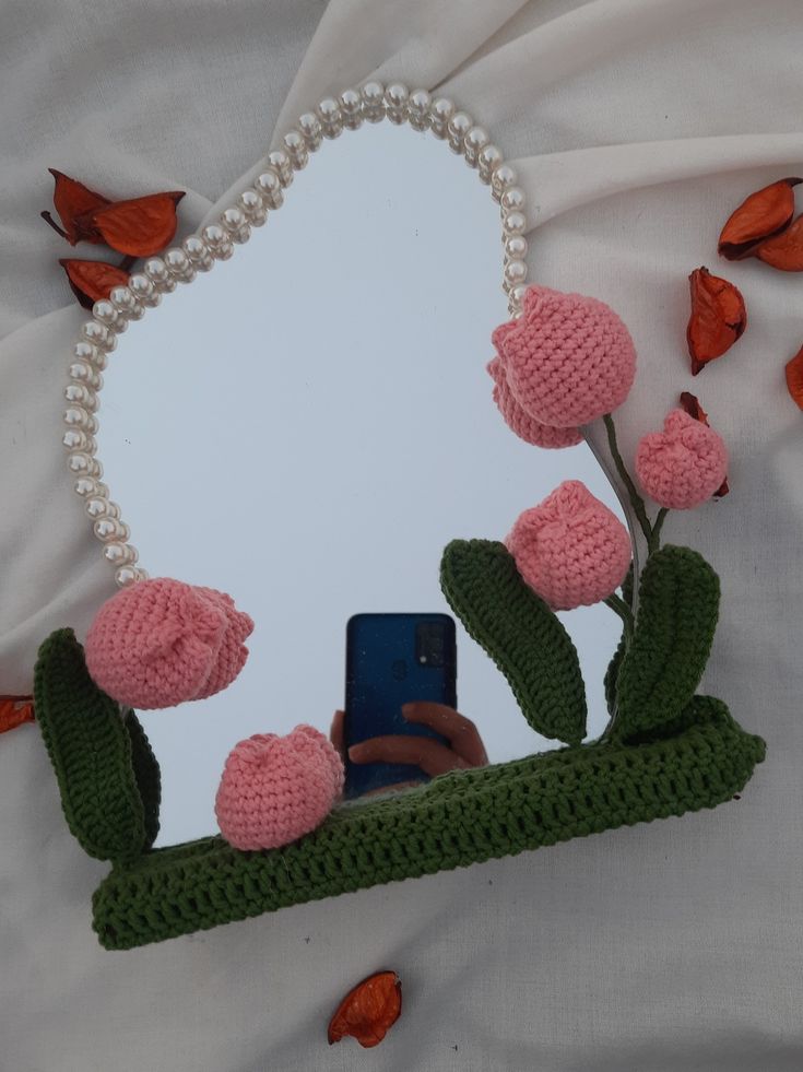 there is a cell phone in front of a mirror with crocheted flowers on it