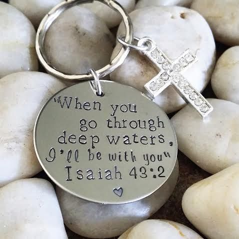 a keychain with a cross and bible verse on it sitting among white rocks