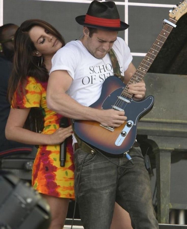 a man playing an electric guitar while standing next to a woman in a colorful dress