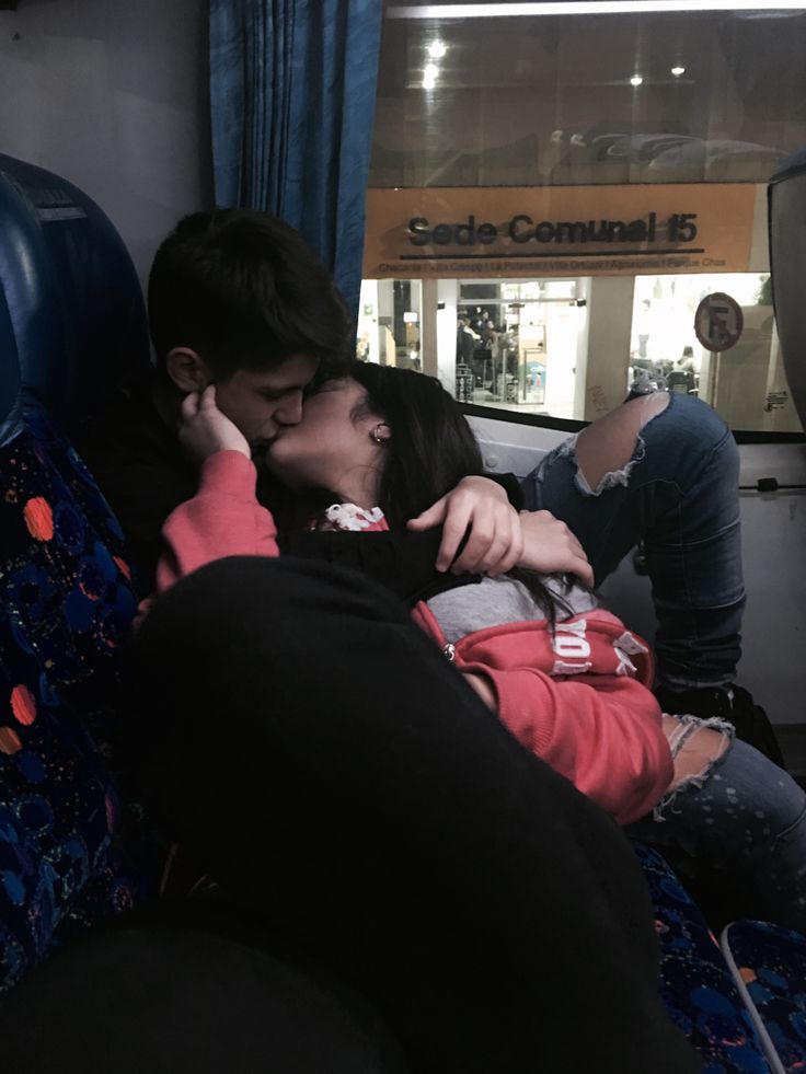 two people sitting on a bus kissing each other while the man is holding his hand up to his face