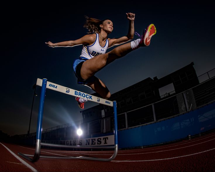 a woman jumping over a hurdle on top of a red and blue race track at night