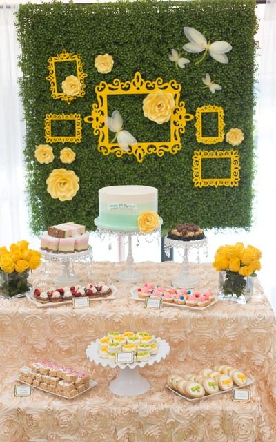 a table topped with cakes and cupcakes next to a wall covered in flowers