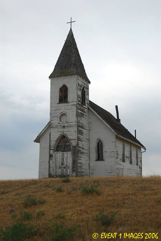 an old white church with a cross on the roof and steeple is standing in a grassy field