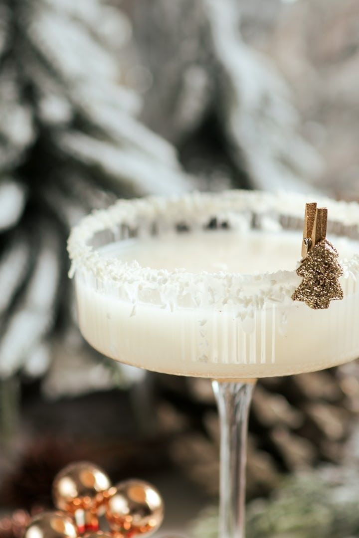 a white cocktail with gold garnish on the rim in front of pine cones