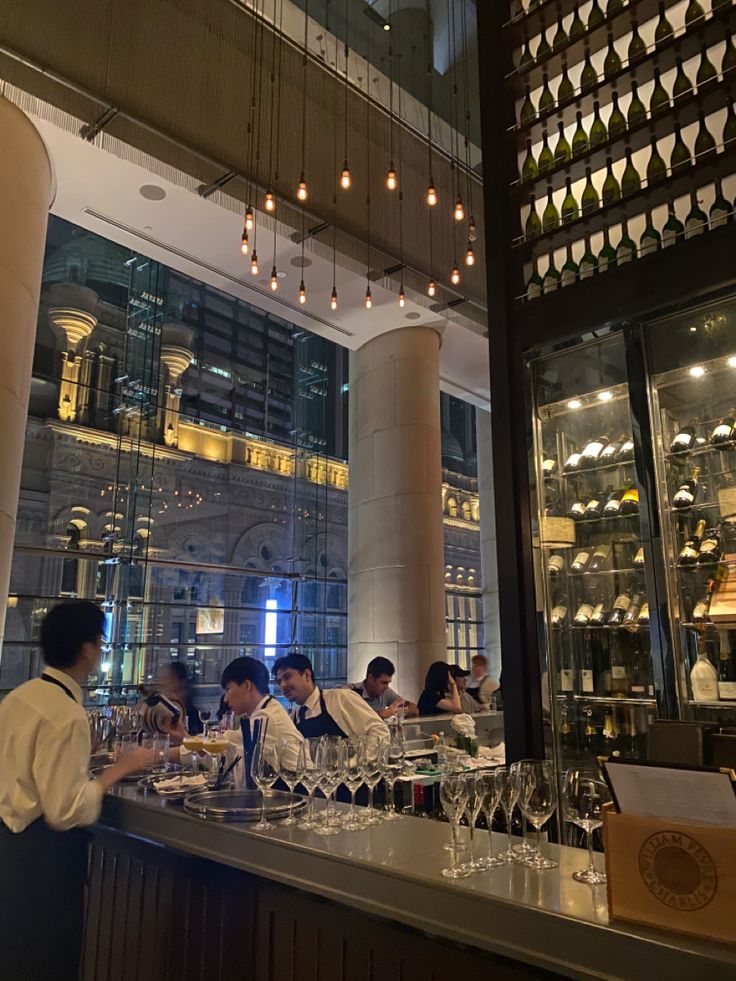 a group of people sitting at a bar with wine glasses on the counter and lights hanging from the ceiling