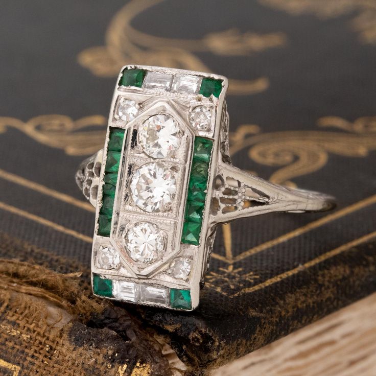 An Art Deco dinner ring studded with Old European cut diamonds, step cuts, and juicy green emeralds! This ring is full of impeccable detail, not to mention she covers up a significant amount of finger real estate! The color combination of diamonds and green emeralds is one that we cannot help but love, especially when set in an original Deco-era beauty. 18kt white gold Size 7.5 & fully resizable Diamond Measures: 5.67 x 5.67 x 3.94 mm Diamonds are estimated to be G/I colors & VVS/VS clarities. G Green Diamond Ring With Single Cut Emerald Shape, Green Emerald Cut Diamond Ring With Single Cut Diamonds, Platinum Emerald Ring With Diamond Accents, Exquisite Green Emerald Platinum Ring, Green Emerald Ring With Diamond Accents In Platinum, Fine Jewelry Green Emerald Ring With Single Cut Diamonds, Gia Certified Art Deco Emerald Ring, Green Art Deco Diamond Ring With Diamond Cut, Green Multi-stone Diamond Ring