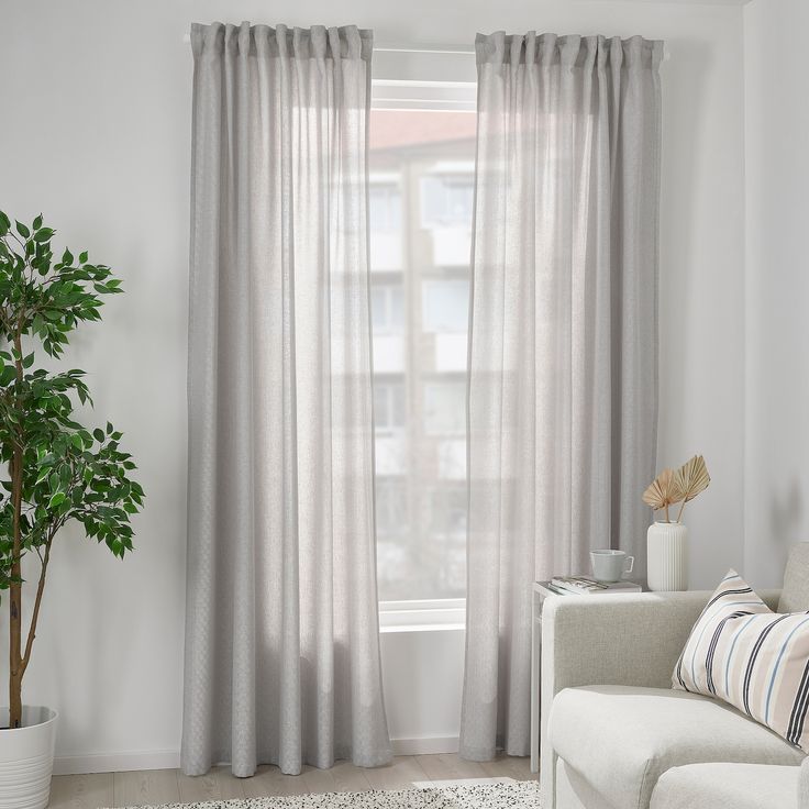 a living room with a white couch and large window covered in sheer curtaining, next to a potted plant